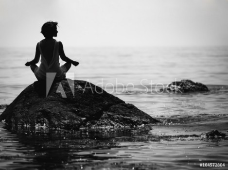 Picture of  young woman sits in a lotus position on a large stone in the sea and meditates her fingers are folded in Prithivi mudra